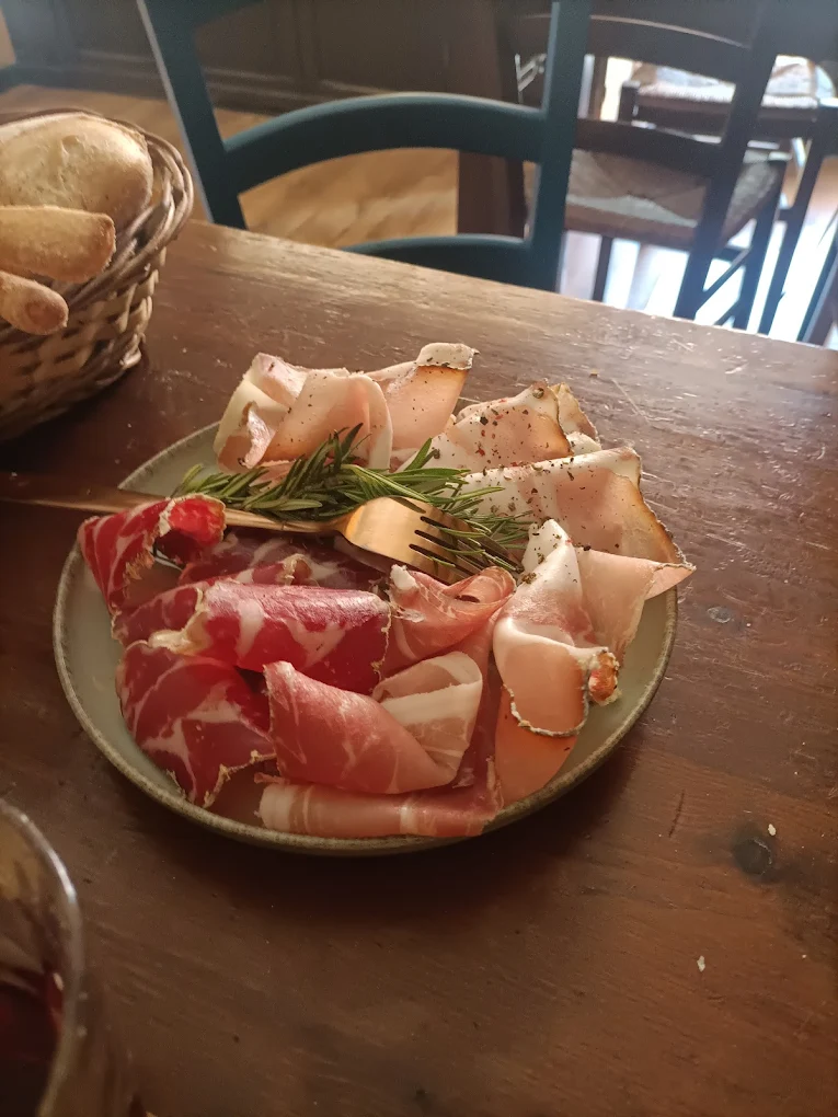 Piatto di prosciutto crudo e coppa con rosmarino, cestino di pane sullo sfondo